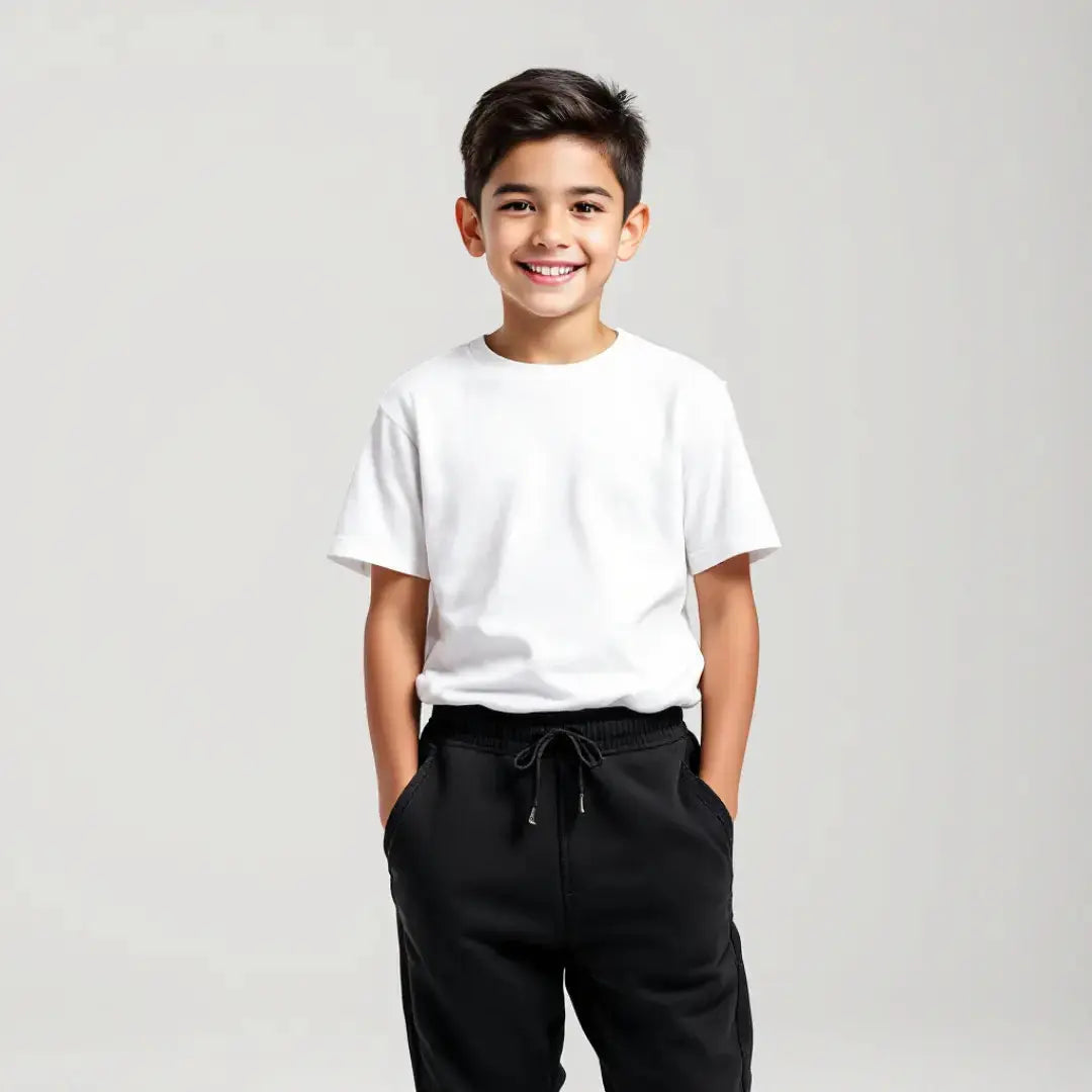 Niño sonriendo con las manos en los bolsillos vistiendo una playera blanca básica de cuello redondo y pantalón deportivo negro, de la colección esencial de Dubrovnik Kids