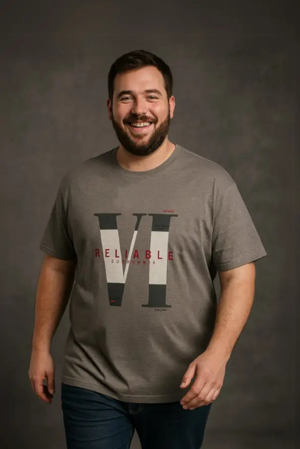 Hombre de complexión robusta sonriendo con una playera gris jaspeada de cuello redondo, con el gráfico "RELIABLE" en rojo y diseño de números romanos, de la colección Tallas Extras de Dubrovnik