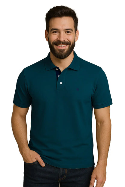 Hombre con barba sonriendo con un polo de manga corta en color azul petróleo profundo, con contraste azul marino en la carterita interna del cuello y escudo bordado, de la marca Dubrovnik