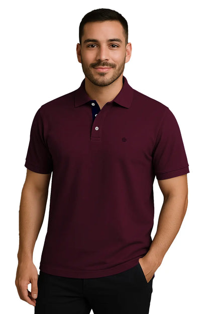 hombre joven con barba vistiendo un polo de manga corta en color borgoña profundo, con contraste azul marino en la carterita interna del cuello y escudo bordado, de la marca Dubrovnik