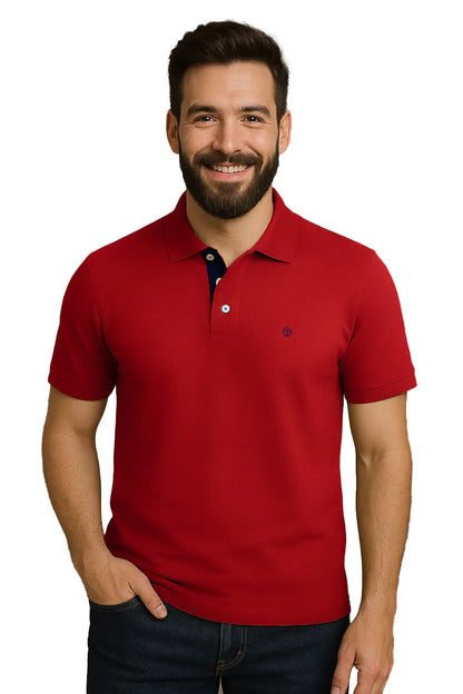 Hombre joven con barba sonriendo con un polo de manga corta en color rojo carmesí vibrante, con contraste azul marino en la carterita interna del cuello y escudo bordado, de la marca Dubrovnik