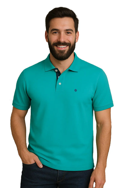 Hombre con barba sonriendo con un polo de manga corta en color verde turquesa vibrante, con contraste azul marino en la carterita interna del cuello y escudo bordado, de la marca Dubrovnik