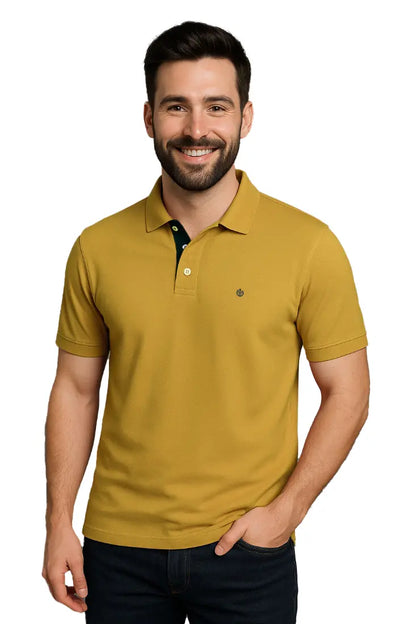 Modelo sonriendo con polo Dubrovnik color mostaza de corte regular, resaltando el detalle de la carterita interna en verde bosque y logotipo bordado en el pecho