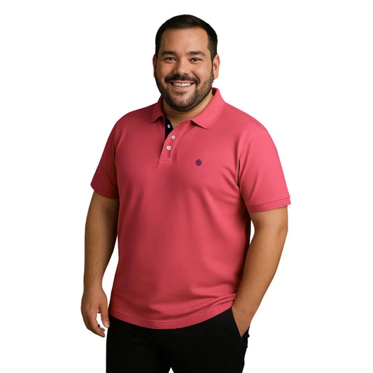 Hombre de complexión robusta sonriendo con polo Dubrovnik color coral o salmón en talla extra, con detalle de carterita en azul marino y escudo bordado