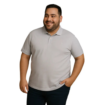 Modelo de complexión robusta sonriendo con polo Dubrovnik color gris perla en talla extra, destacando el ajuste cómodo en hombros y el escudo bordado a tono