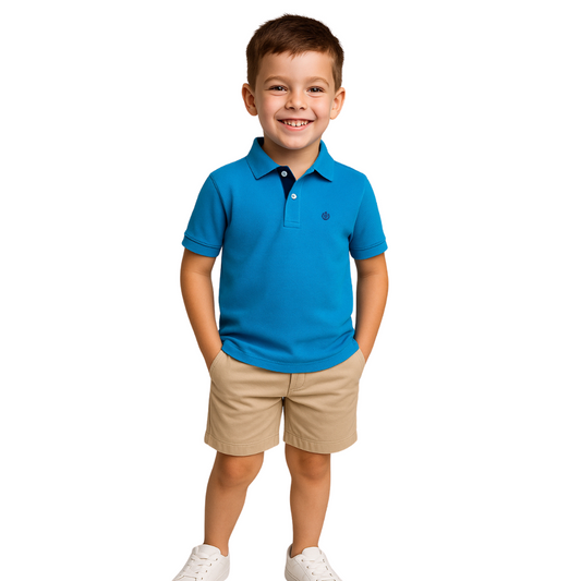 Niño sonriendo con las manos en los bolsillos, vistiendo un polo de manga corta en color azul real con detalles en azul marino y bermudas beige, de la marca Dubrovnik Kids
