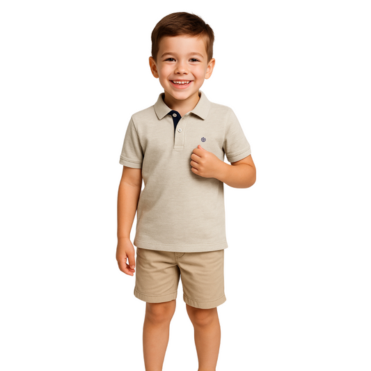 Niño sonriendo con un polo de manga corta en color arena jaspeado, con contraste azul marino en el cuello y el logotipo de escudo bordado en el pecho, de la colección Dubrovnik Kids