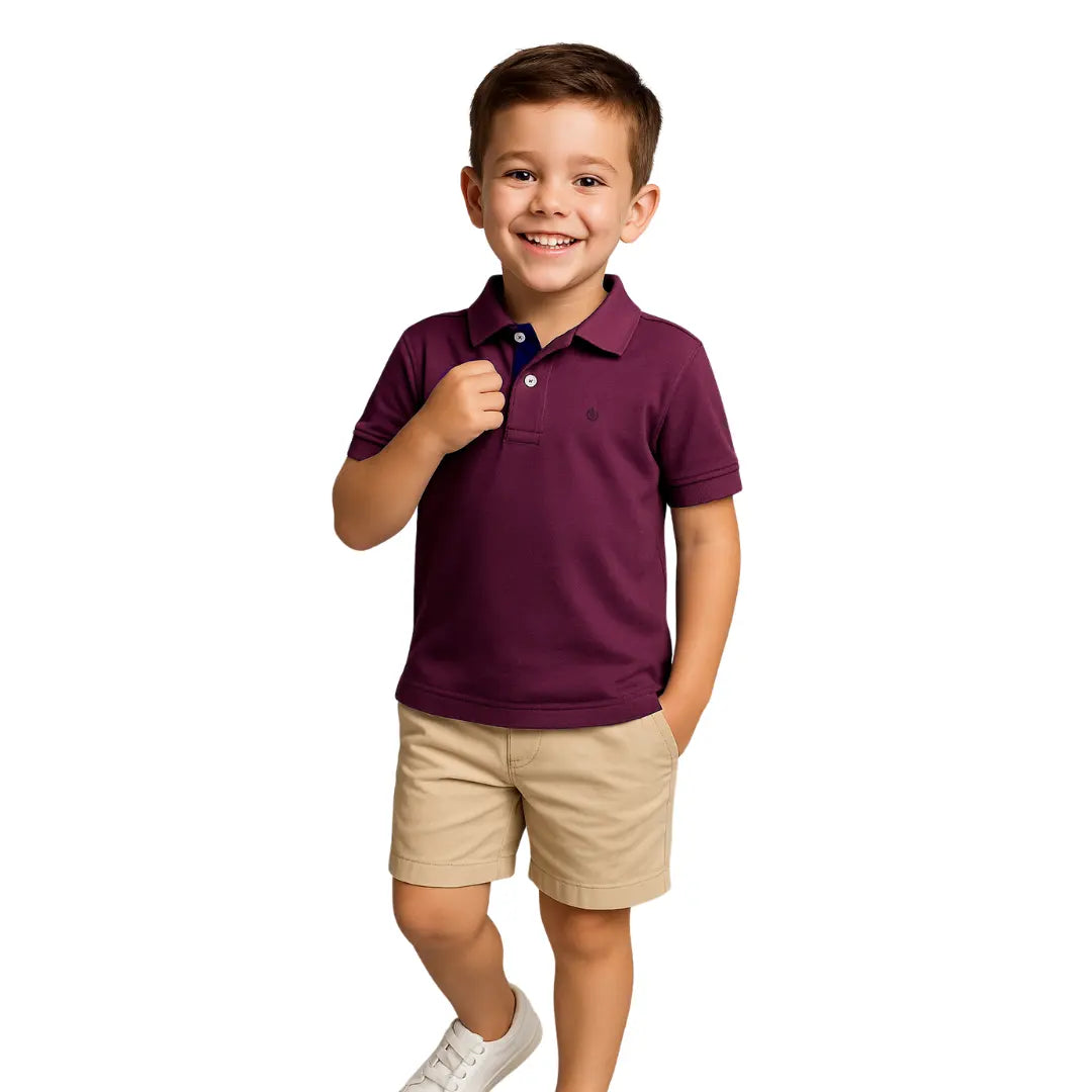 Niño sonriendo con un polo de manga corta en color ciruela (púrpura oscuro) con detalles en azul marino, combinado con bermudas beige, de la línea infantil de Dubrovnik.