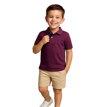 Niño sonriendo con un polo de manga corta en color ciruela (púrpura oscuro) con detalles en azul marino, combinado con bermudas beige, de la línea infantil de Dubrovnik.