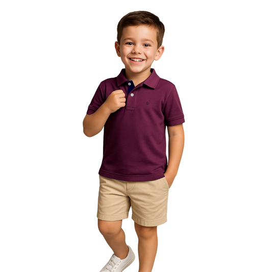 Niño sonriendo con un polo de manga corta en color ciruela (púrpura oscuro) con detalles en azul marino, combinado con bermudas beige, de la línea infantil de Dubrovnik.