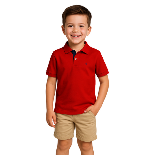 Niño sonriendo con un polo de manga corta en color rojo vibrante con detalles en azul marino en el cuello, combinado con bermudas beige, de la marca Dubrovnik Kids