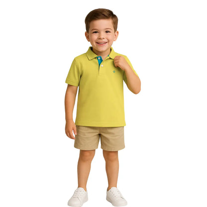 Niño sonriendo con un polo de manga corta en color verde lima con detalles turquesa en el cuello, combinado con bermudas beige, de la colección Dubrovnik Kids