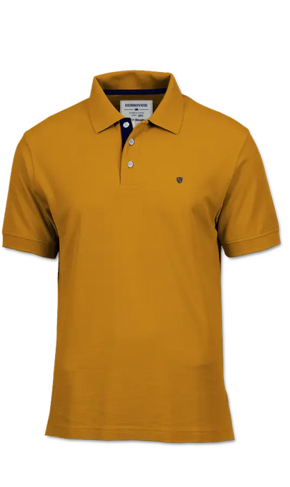 Polo de piqué Dubrovnik en color mostaza, destacando el contraste azul marino en el cuello interno, botones blancos de alta resistencia y escudo bordado en marino